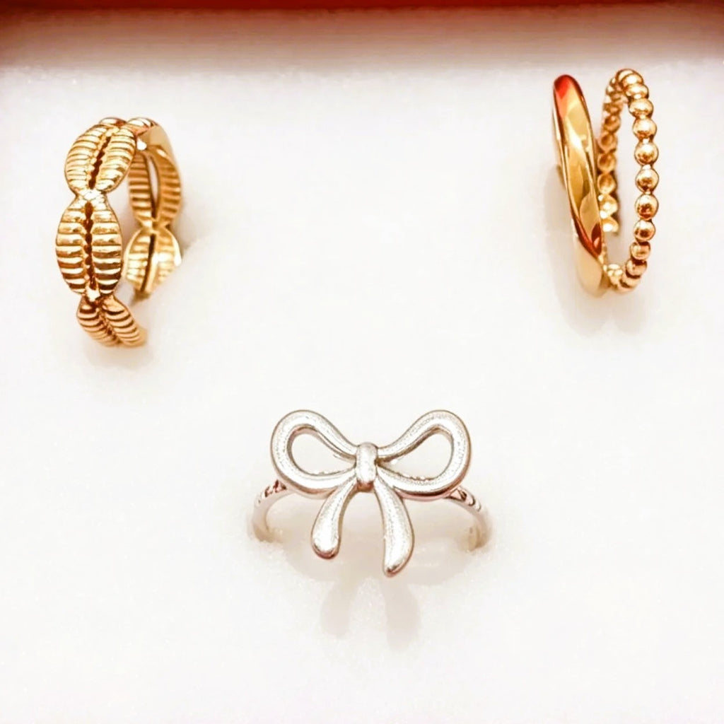 Three gold and silver rings displayed on a white background: two gold rings at the top and a silver bow ring at the bottom center.